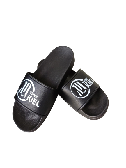 Ein Paar schwarze Badeschlappen mit weißem THW KIEL-Logo auf den Trägern, ideal zum Entspannen in der Sauna, auf weißem Hintergrund.