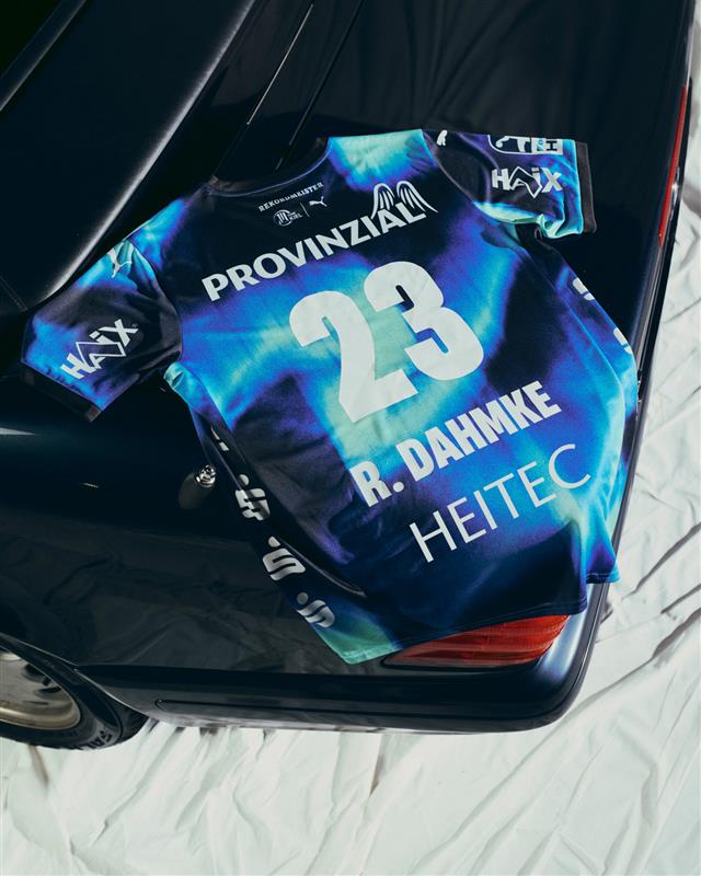 Ein THW Kiel 25-26 Auswärtstrikot Jr PUMA Navy mit der Nummer 23 und dem Namen R. Dahmke ruht auf einem dunklen Autokofferraum. Das farbenfrohe Trikot ist mit Sponsorenlogos versehen und wird auf einem weißen Laken präsentiert.