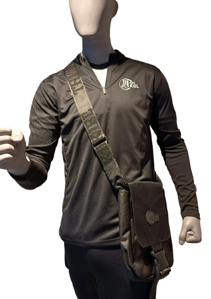 Eine Schaufensterpuppe trägt ein schwarzes Langarm-Sportshirt mit THW-Kiel-Logo, eine passende schwarze Hose und die Cross Body Bag BUCKLE schwarz mit breitem Riemen und praktischem Reißverschluss.