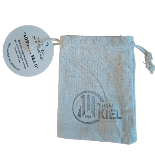 Eine kleine beigefarbene Kordeltasche mit THW Kiel 1904 und einem runden Anhänger mit der Aufschrift "Your piece of the magnet Adria Sea IV, Handmade in Germany" - ideal zur Aufbewahrung Ihres Bracenet Schlüsselanhänger II weiße Kordel.