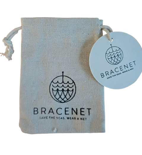 Ein beiger Kordelzugbeutel mit dem Bracenet-Logo und dem Text "SAVE THE SEAS. WEAR A NET." enthält einen runden Bracenet-Anhänger und den Bracenet Schlüsselanhänger II weiße Kordel.
