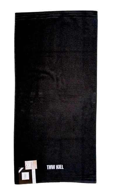 Ein schwarzes Handtuch (50 x 100 cm) von Vossen mit weißer THW Kiel-Stickerei am unteren Rand und zwei Produkt-Tags an einer Ecke.