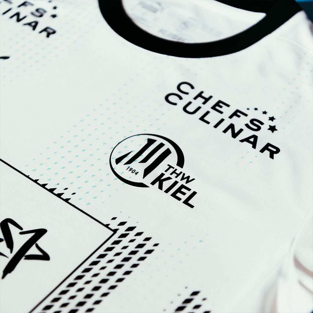 Nahaufnahme des THW Kiel 24-25 Heimtrikots von PUMA in Weiß mit dem CHEFS CULINAR Logo, dem Vereinswappen, schwarzen Akzenten und dem charakteristischen Zebra-Design mit geometrischen Elementen.