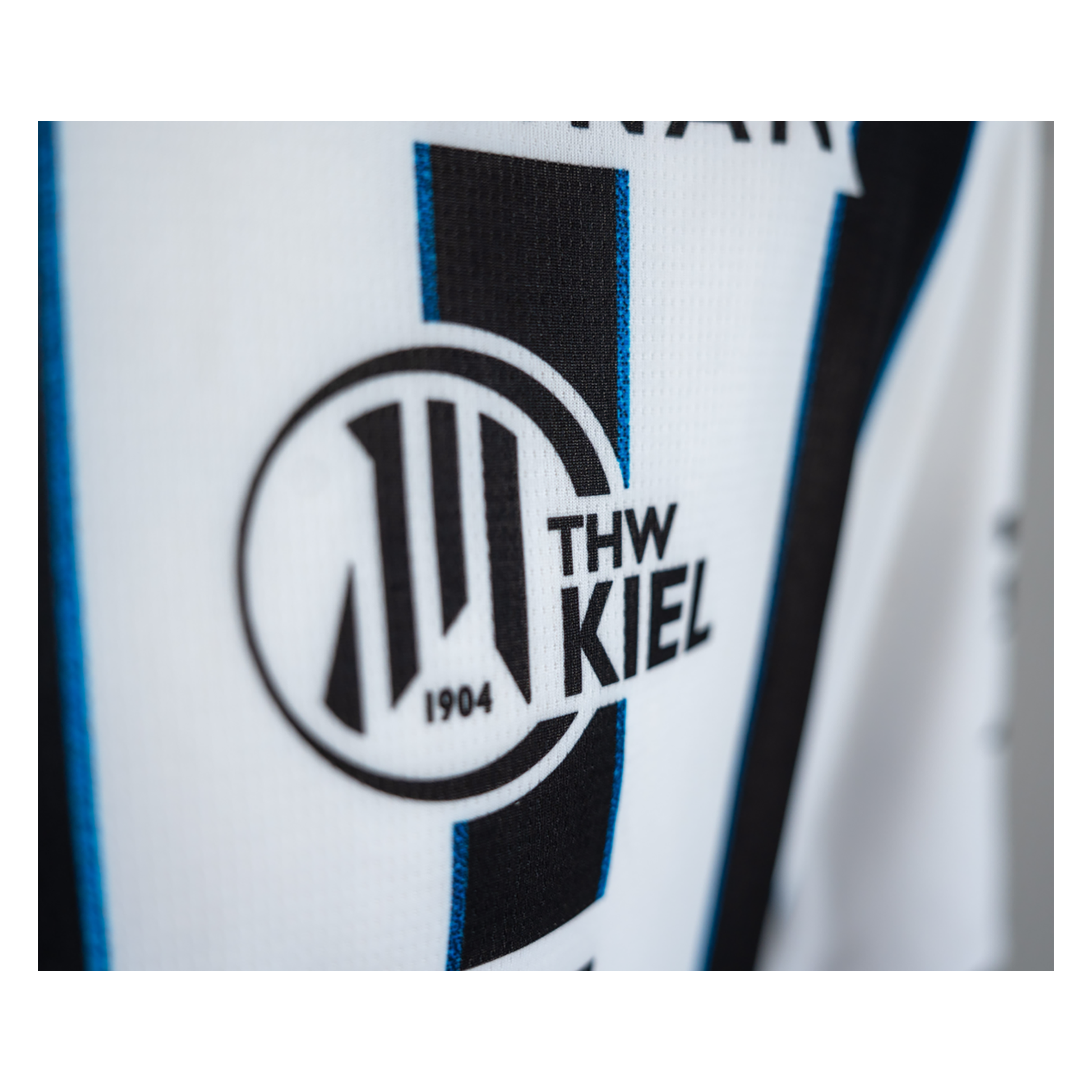 Nahaufnahme des THW Kiel 25-26 Heimtrikots von PUMA in Weiß. Zu sehen sind das kultige Zebras-Logo, der Vereinsname und "1904" in einem runden Abzeichen mit Streifenmuster.