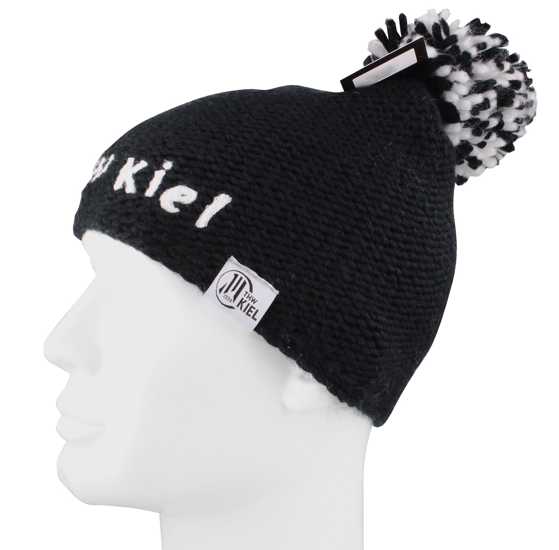 Die Pudelmütze THW KIEL gestrickt schwarz ist eine schwarze Strickmütze mit weißem Logoaufnäher, gesticktem Schriftzug und schwarz/weißem Bommel - abgebildet auf einem weißen Puppenkopf im Profil - perfekt als Handball-Accessoire.