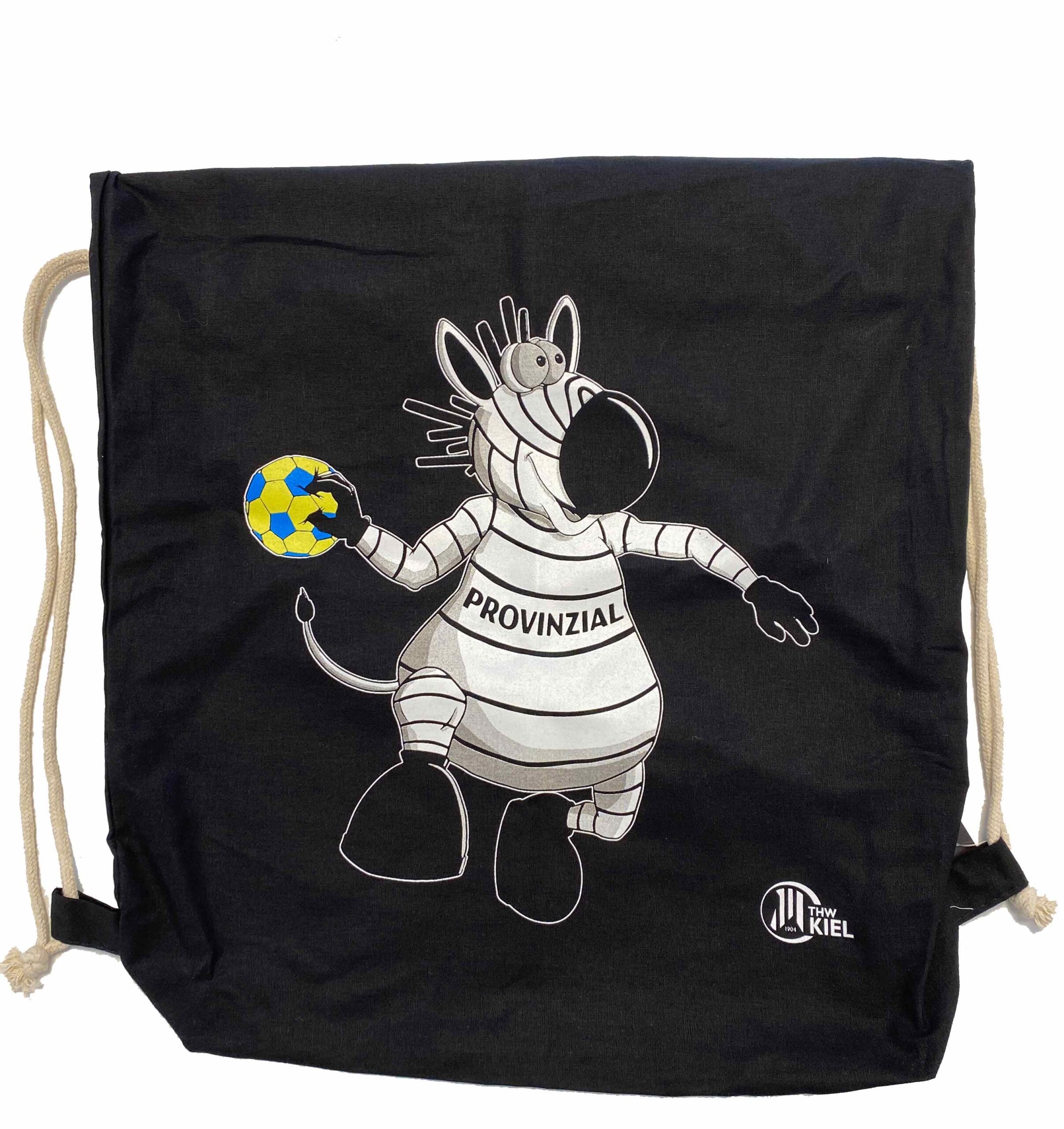 Der Turnbeutel Hein Daddel Sprungwurf schwarz ist ein schwarzer Baumwollturnbeutel mit einem sportlichen Zebra im Provincia-Trikot, das einen blau-gelben Handball hält, mit dem THW Kiel-Logo in der rechten unteren Ecke.