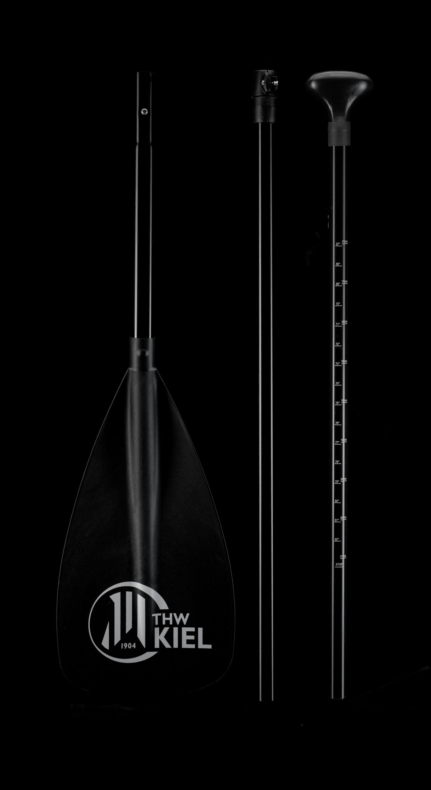 Drei schwarze Kajakpaddelteile vor schwarzem Hintergrund: ein THW Kiel SUP limitiert Blatt, Mittelschaft und Griff mit Markierungen - ideal für Stand-up Paddling-Enthusiasten oder Ihre exklusive limitierte SUP-Sammlung.