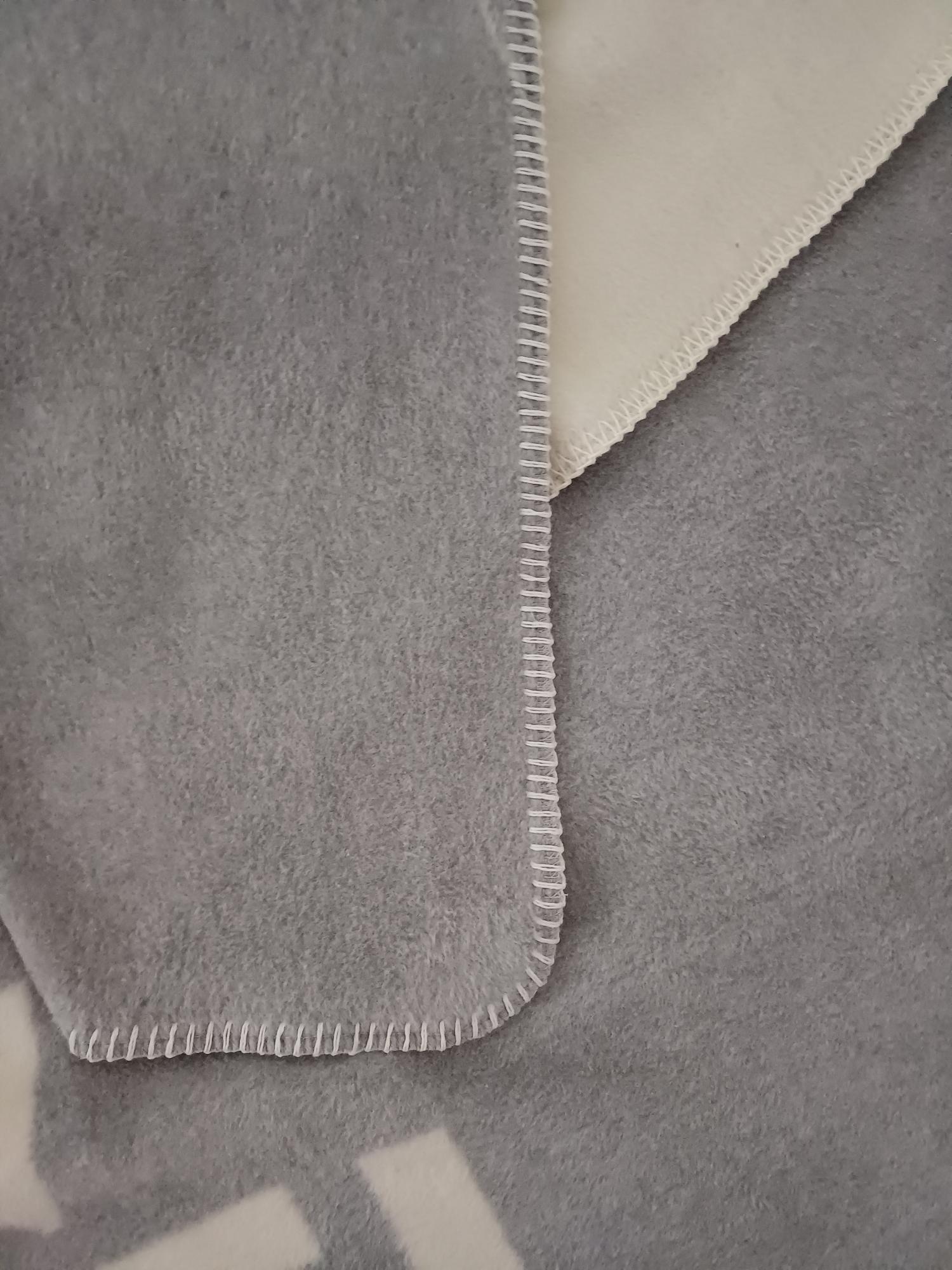 Eine Nahaufnahme der Kuscheldecke Linien grau-beige zeigt den Rand mit weißer Overlocknaht und hebt den Kontrast zwischen den grauen und beigen Seiten hervor.