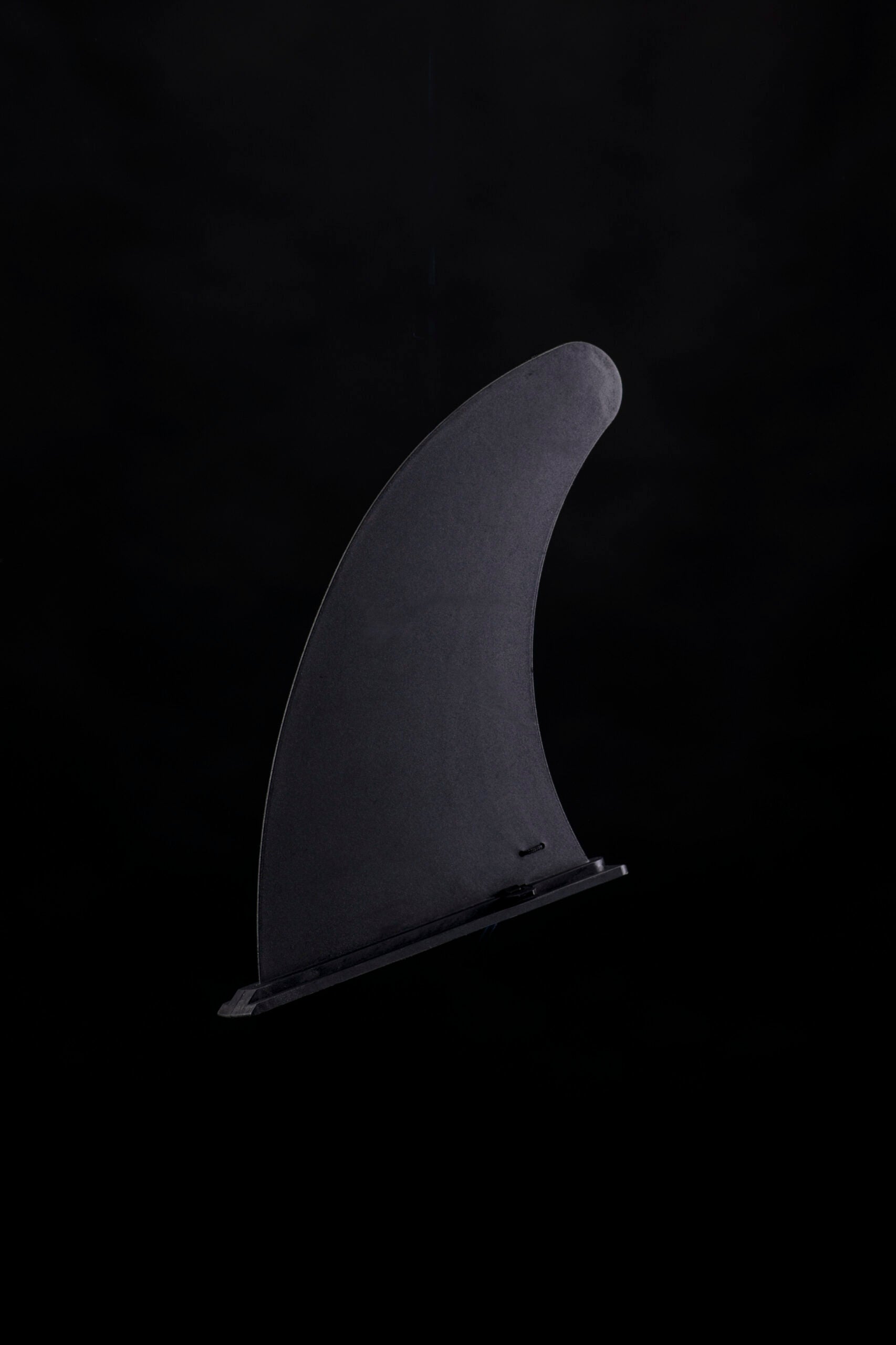 Eine einzelne schwarze Surfboard-Finne, perfekt für das THW Kiel SUP limitiert Board, steht aufrecht vor einem dunkelschwarzen Hintergrund.