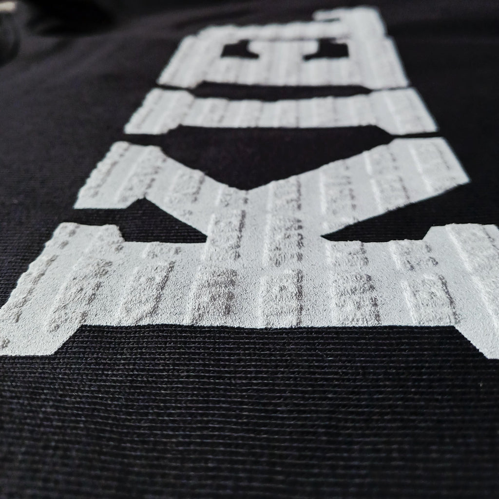 Nahaufnahme eines verpixelten weißen Roboters auf strukturierter Bio-Baumwolle, gedruckt auf den Hoodie 3D Print in schwarz. Das lächelnde Design mit zwei Augen und einem rechteckigen Kopf ist ideal für THW KIEL Fans.