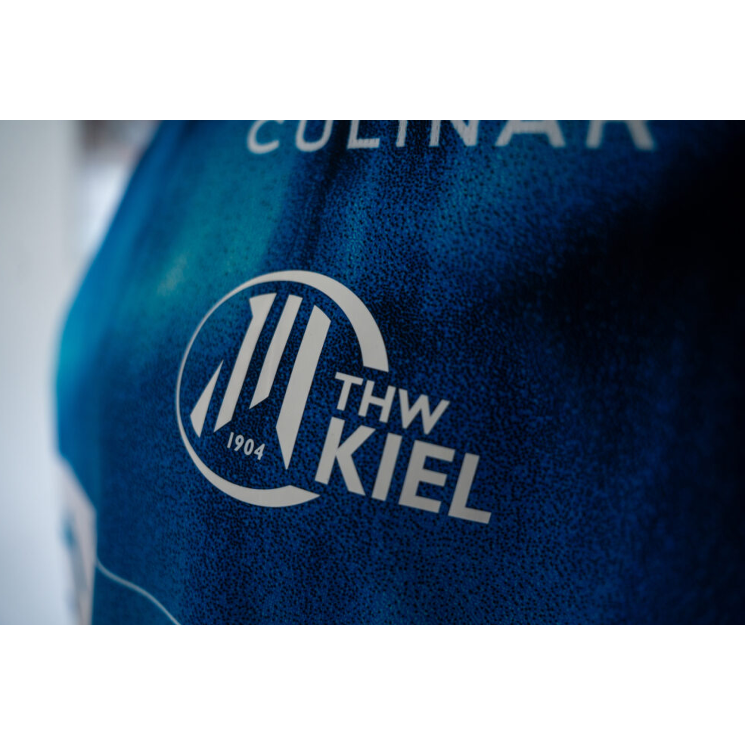 Nahaufnahme des THW Kiel 25-26 Auswärtstrikots von PUMA in navy, mit dem weißen THW Kiel-Logo mit "1904" und stilisierten Kreislinien sowie einem Teil des Textes "CULINAR" darüber.
