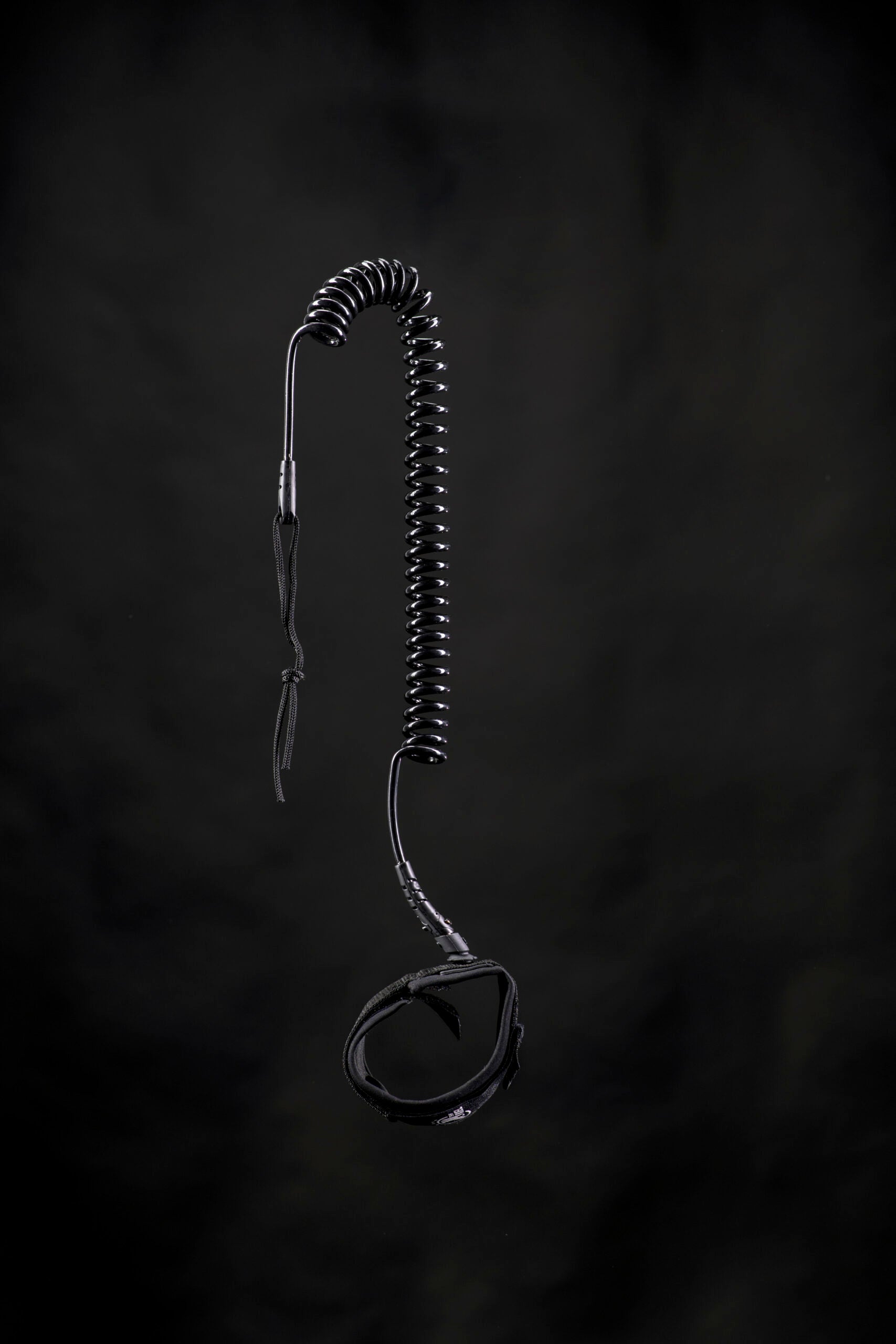 Ein schwarzes Spiralkabel mit einem Ohrhörer und einem Clip, der an ein Funkgerät erinnert, hängt vor einem dunklen Hintergrund - genau wie die Ausrüstung, die Sie am Wasser mit Ihrem THW Kiel SUP limitiert Board verwenden würden.