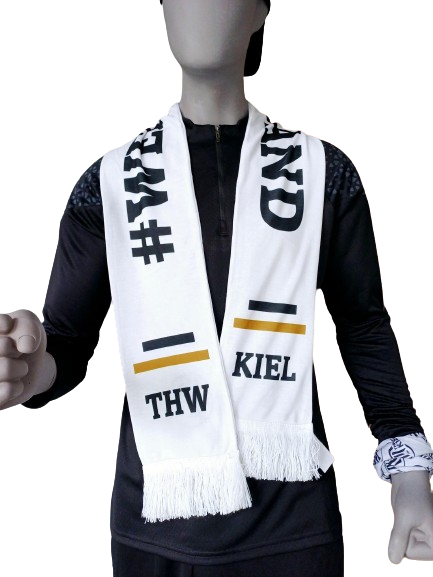 Eine Schaufensterpuppe trägt ein schwarzes langärmeliges Oberteil und den Schal weissewand weiß mit "THW KIEL", schwarzen und gelben Streifen aus Baumwollstoff, Fransen sowie ein weißes Stoffband am linken Handgelenk zur Unterstützung der Mannschaft.