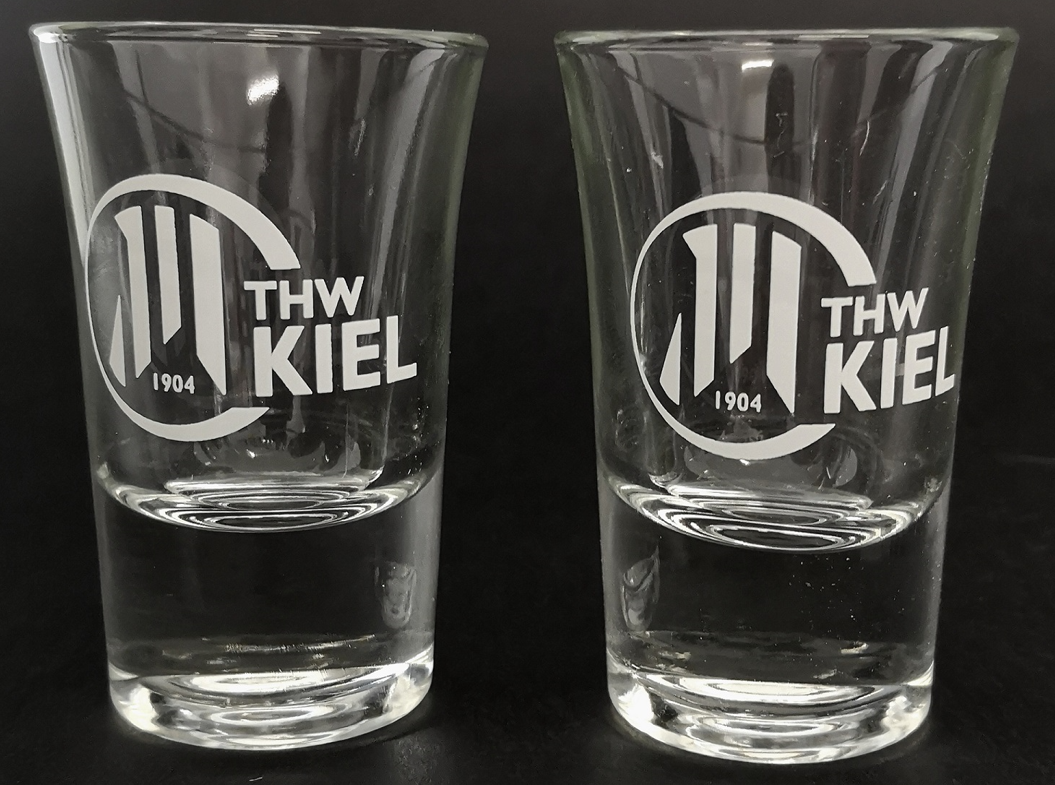 Zwei klare Schnapsgläser 2er mit THW Kiel Logo und 1904 in Weiß nebeneinander vor schwarzem Hintergrund - das perfekte Handball-Fanartikel oder Geschenk für echte Fans.
