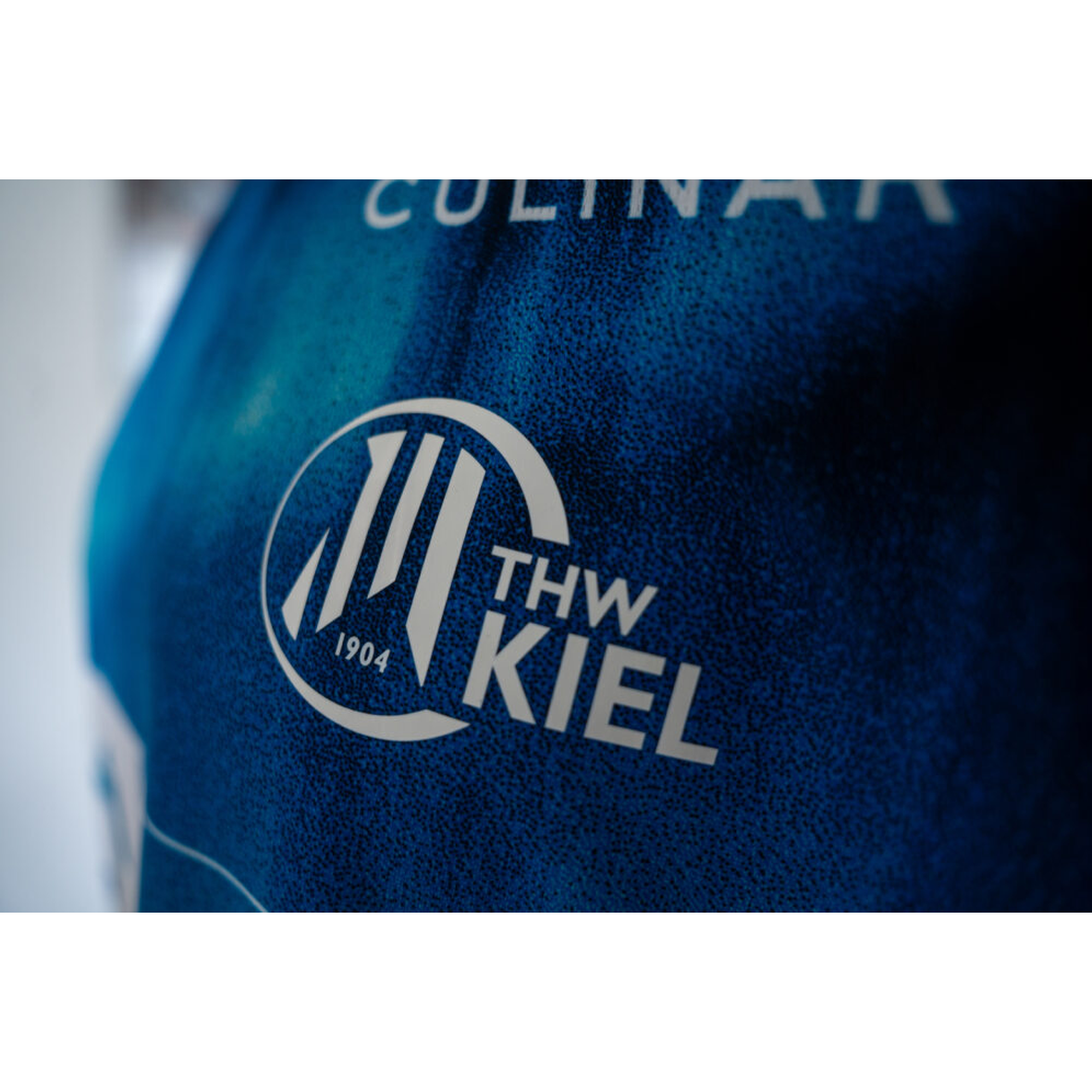 Nahaufnahme des THW Kiel 25-26 GK Trikots Home by PUMA in Marineblau. Zu sehen ist ein weißes, rundes THW Kiel 1904-Logo mit drei stilisierten Linien und dem teilweise sichtbaren Wort CULINAR darüber.