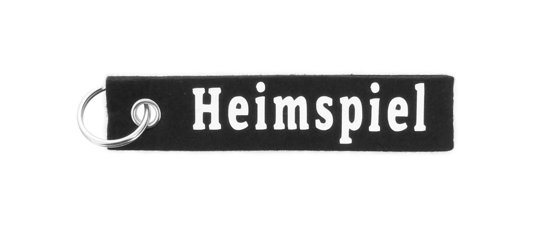 Der Schlüsselfilz ist ein schwarzer, rechteckiger Filz-Schlüsselanhänger mit einem silbernen Schlüsselring, auf dem "Heimspiel" in fetten weißen Buchstaben steht.